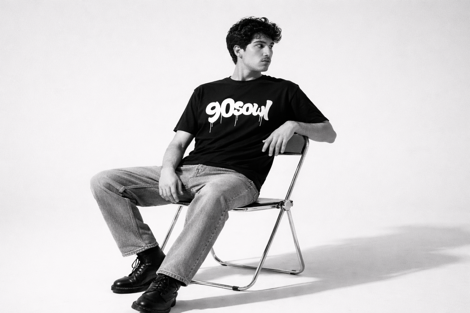 Model sitting on a chair wearing a black oversized graphic t-shirt with relaxed denim in monochrome retro streetwear style by 90sOWL