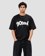 A man wearing a black crewneck t-shirt with a white '90soul' graphic printed across the chest, paired with black jeans, against a light gray studio background.