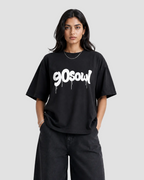 A woman modeling an oversized black t-shirt with a white '90soul' graphic printed across the chest, paired with black wide-leg jeans, against a plain light gray background.