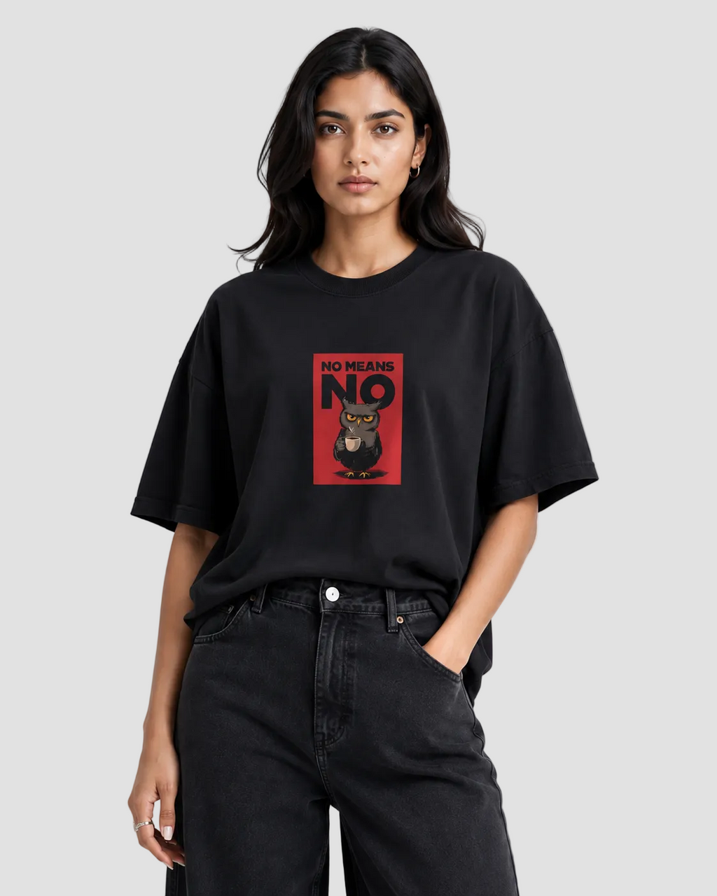 A woman modeling an oversized black t-shirt with a red graphic print on the front featuring the text 'NO MEANS NO' and an owl illustration. She is wearing black jeans against a plain light gray studio background.