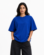 A woman modeling an oversized short-sleeve crewneck t-shirt in a vibrant royal blue color, paired with black wide-leg jeans, against a plain white studio background.