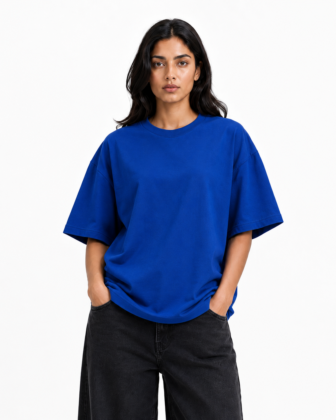 A woman modeling an oversized short-sleeve crewneck t-shirt in a vibrant royal blue color, paired with black wide-leg jeans, against a plain white studio background.