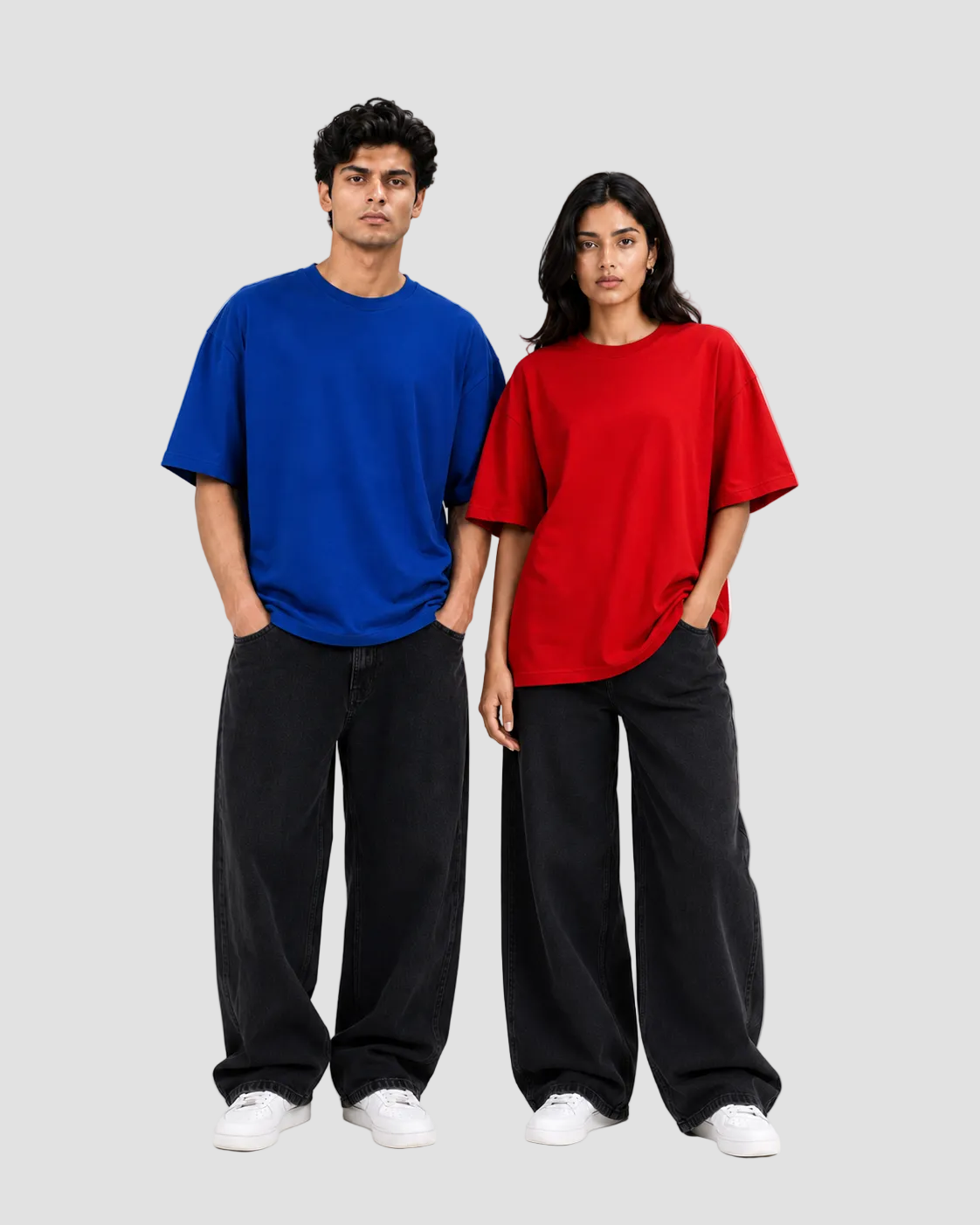 A man and a woman modeling oversized short-sleeve t-shirts in vibrant royal blue and bright red, paired with loose black pants and white sneakers, against a plain white studio background.