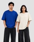 Two models standing side-by-side wearing oversized short-sleeve crewneck t-shirts, one in vibrant royal blue and the other in cream beige, paired with dark wide-leg jeans against a plain white studio background.
