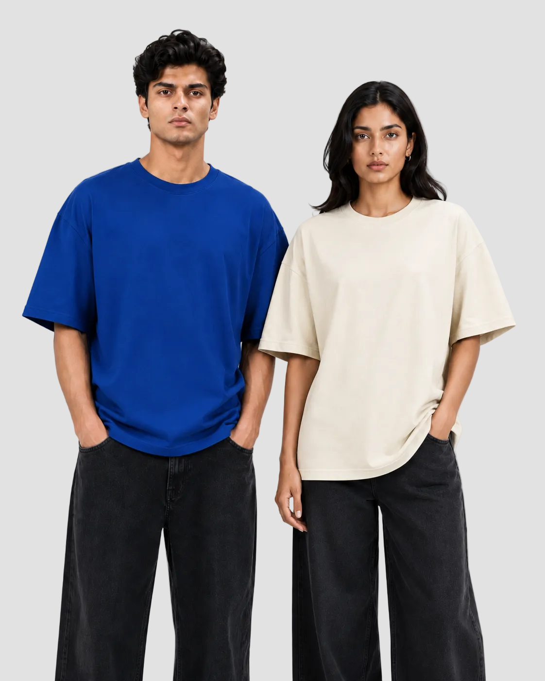 Two models standing side-by-side wearing oversized short-sleeve crewneck t-shirts, one in vibrant royal blue and the other in cream beige, paired with dark wide-leg jeans against a plain white studio background.