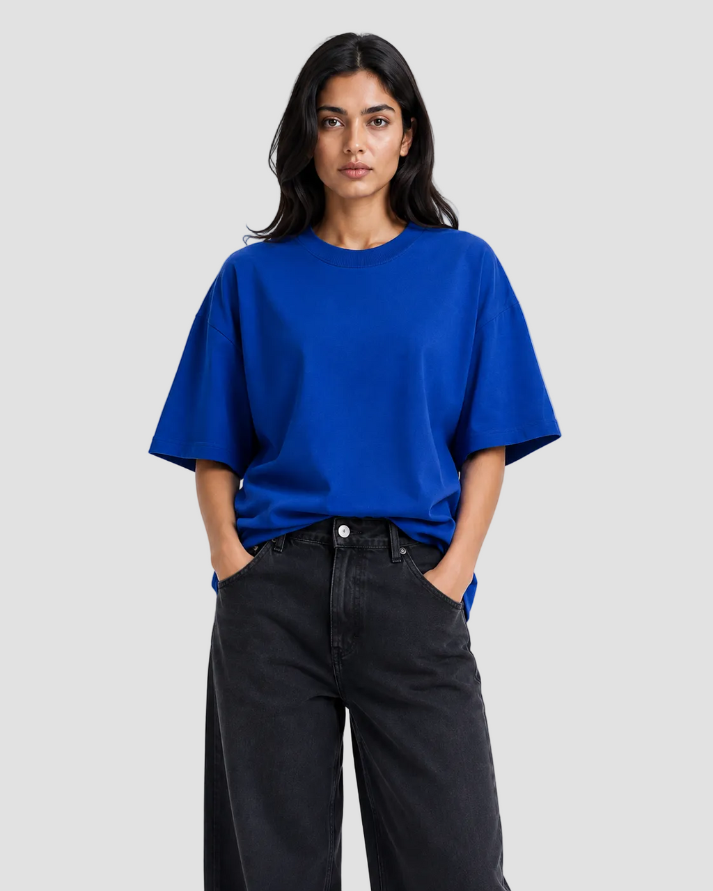 A woman modeling a vibrant royal blue oversized short-sleeve t-shirt paired with black wide-leg jeans, set against a plain white studio background.