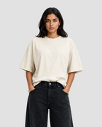 A woman modeling an oversized cream-colored short-sleeve t-shirt paired with black wide-leg jeans, set against a plain white studio background.