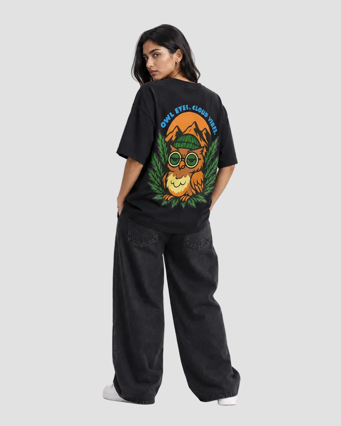 A model shown from the back wearing a black oversized graphic t-shirt with a colorful owl design and the text 'OWL. FTTL.