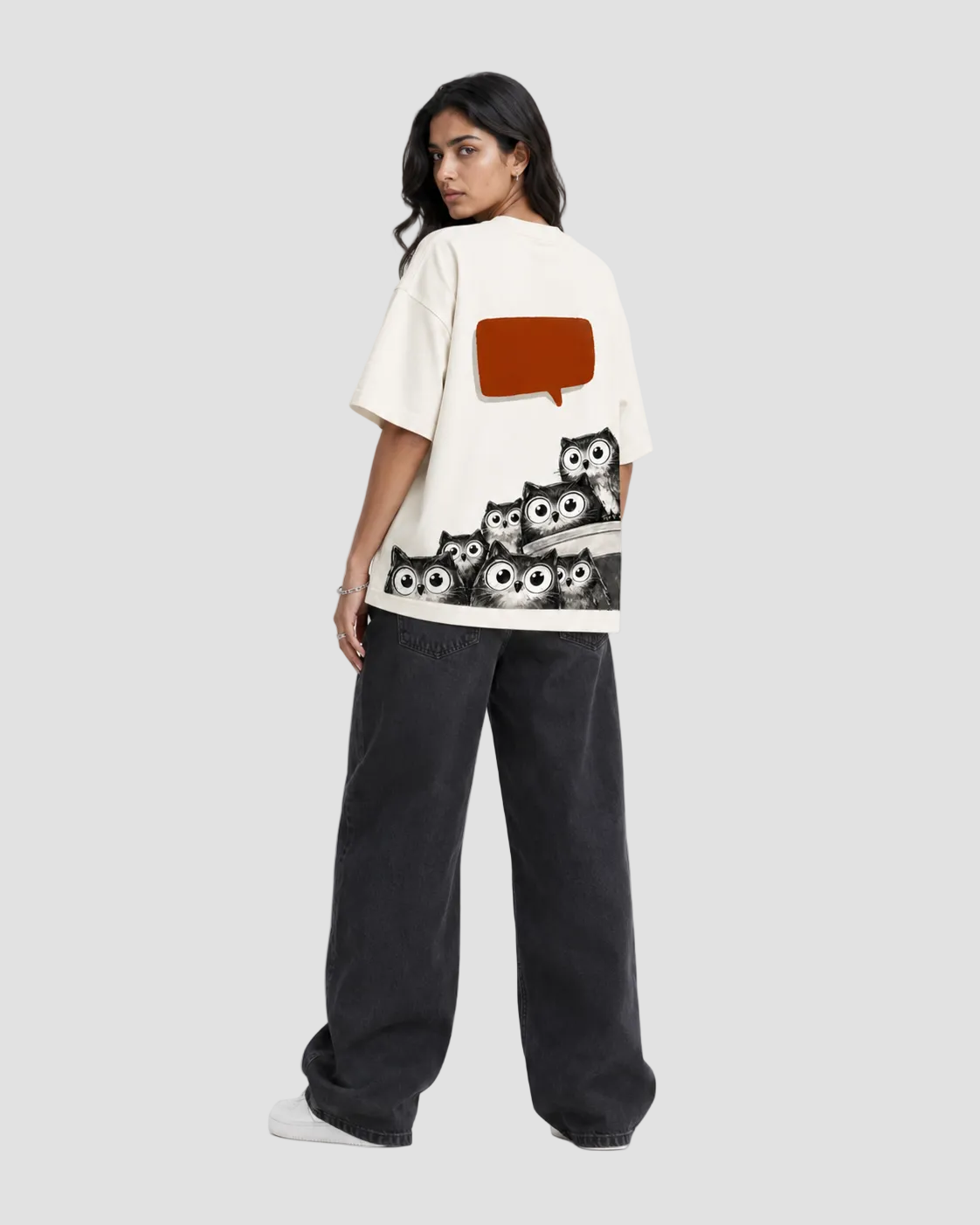 A model shown from the back wearing an off-white graphic t-shirt with a brown speech-bubble-shaped pocket and a black-and-white owl print along the hem, paired with dark charcoal wide-leg jeans.