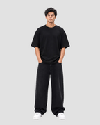 A man modeling a black oversized short-sleeve t-shirt and matching black wide-leg sweatpants, paired with white sneakers, against a solid white background.