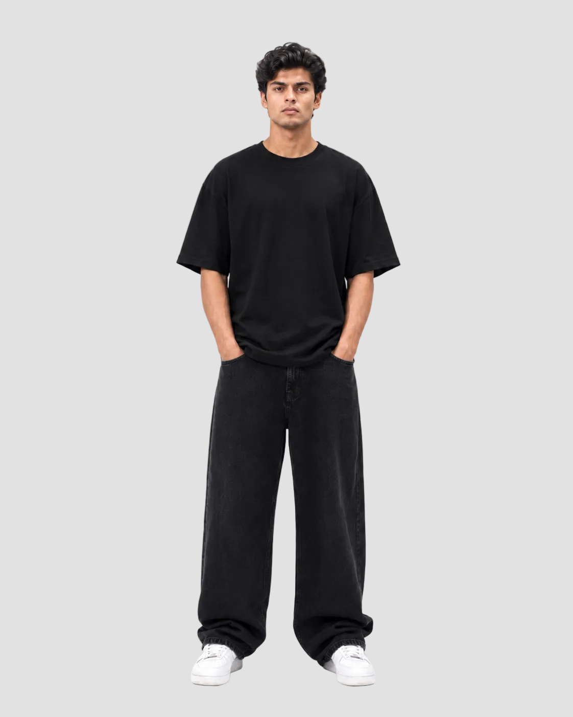 A man modeling a black oversized short-sleeve t-shirt and matching black wide-leg sweatpants, paired with white sneakers, against a solid white background.