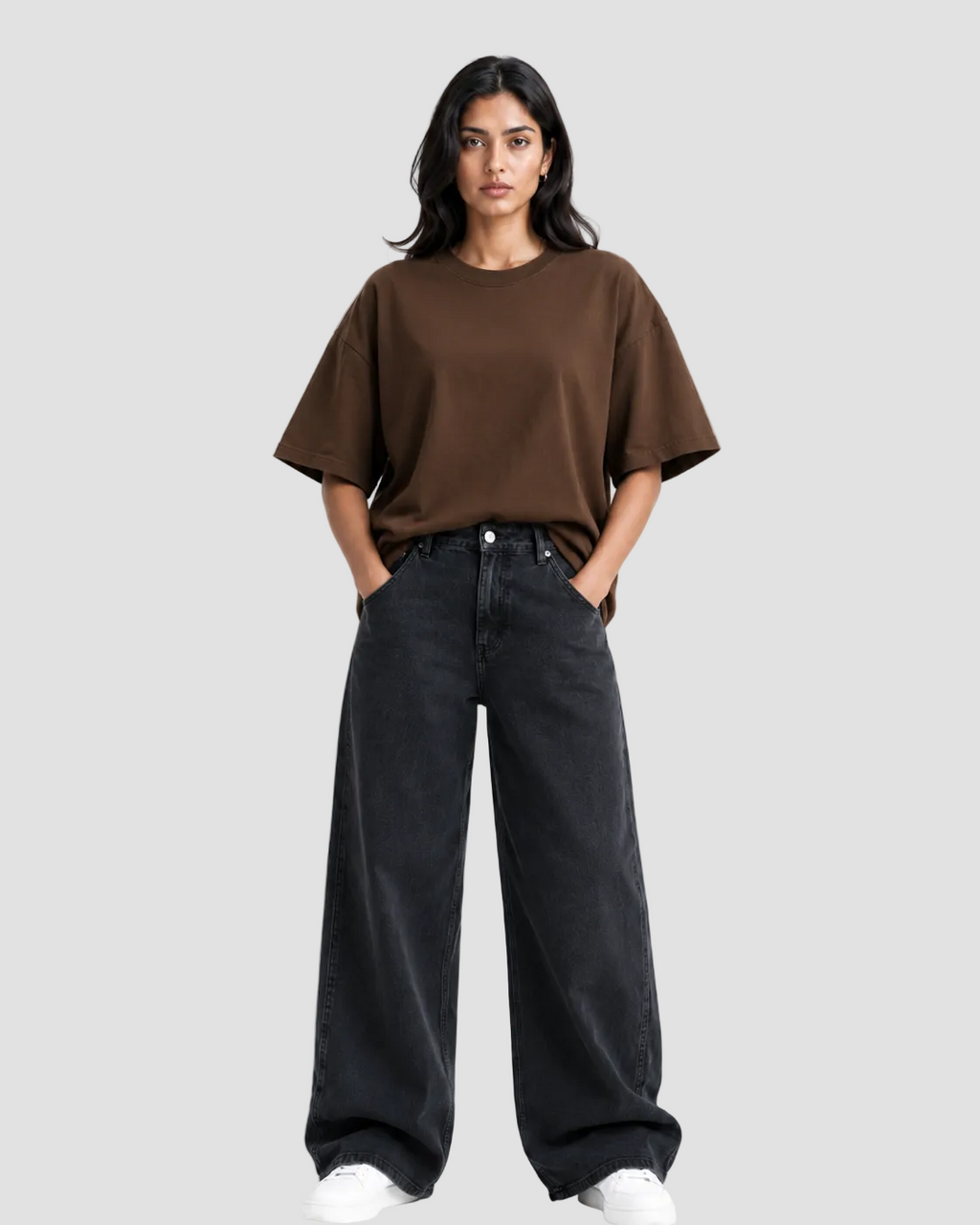 A woman modeling a brown short-sleeve crewneck t-shirt paired with wide-leg black jeans and white sneakers, standing against a plain white studio background.