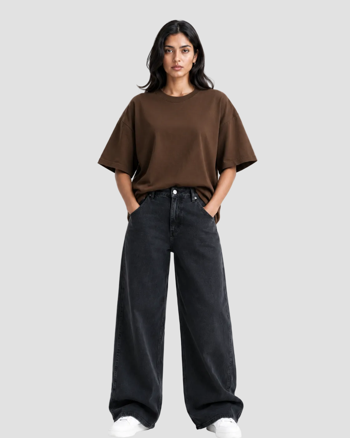 A woman modeling a brown short-sleeve crewneck t-shirt paired with wide-leg black jeans and white sneakers, standing against a plain white studio background.