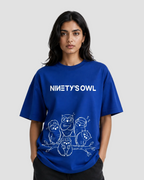 A woman modeling a royal blue oversized t-shirt with a white graphic print of five owls and the text 'NINETY'S OWL' on the front, set against a plain light gray background.