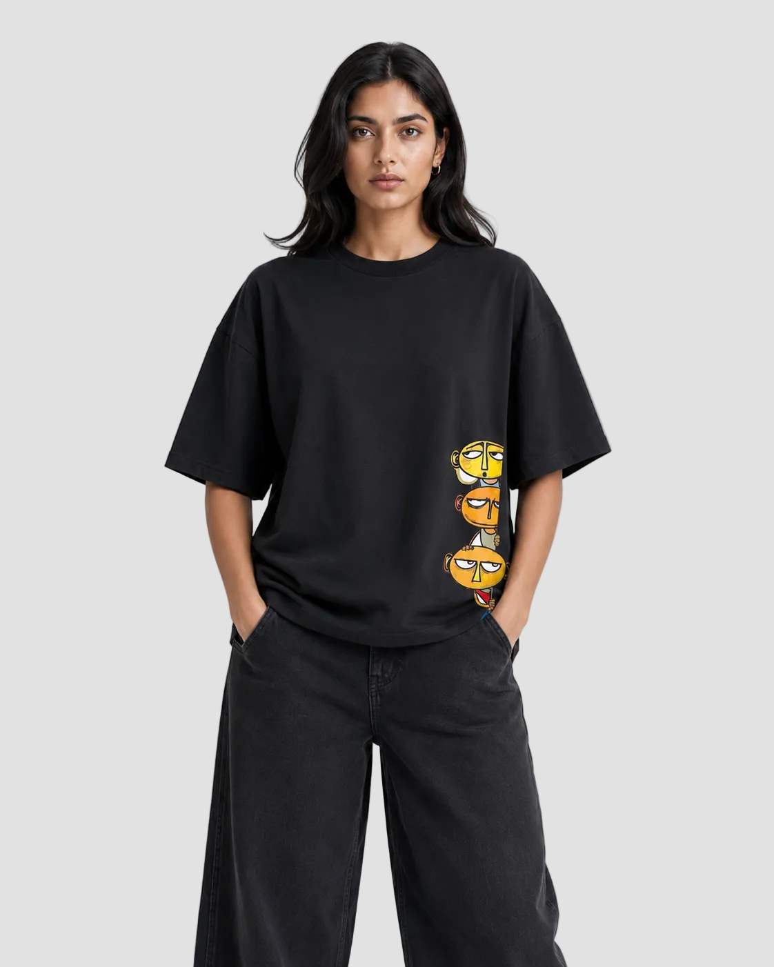 A woman modeling a black oversized short-sleeve t-shirt with a vertical graphic print of three cartoon eyes in yellow, orange, and red on the lower right side, paired with black wide-leg jeans against a light gray studio background.
