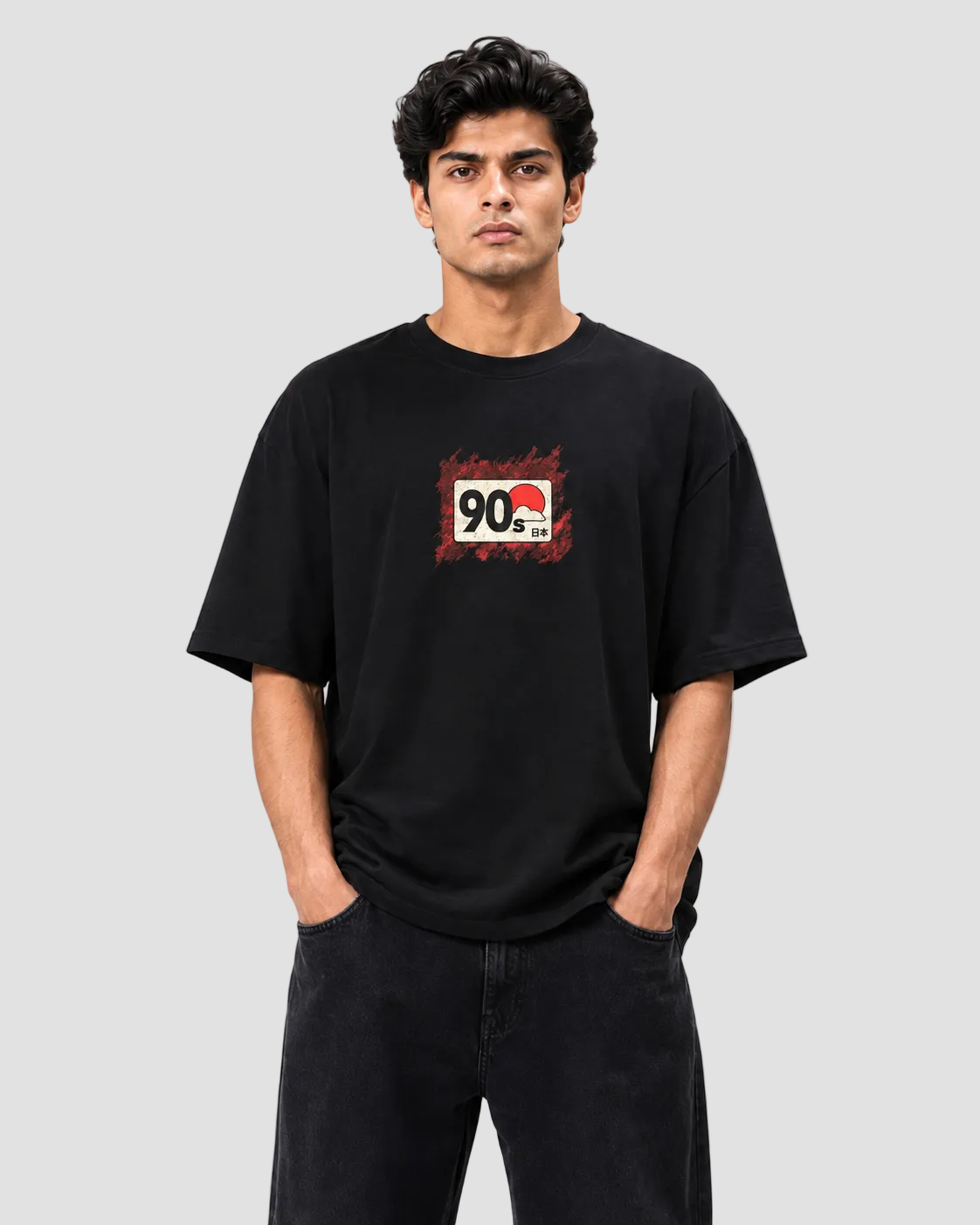 A man wearing a black short-sleeve t-shirt with a red and white graphic print on the chest, paired with black jeans, against a plain white background.