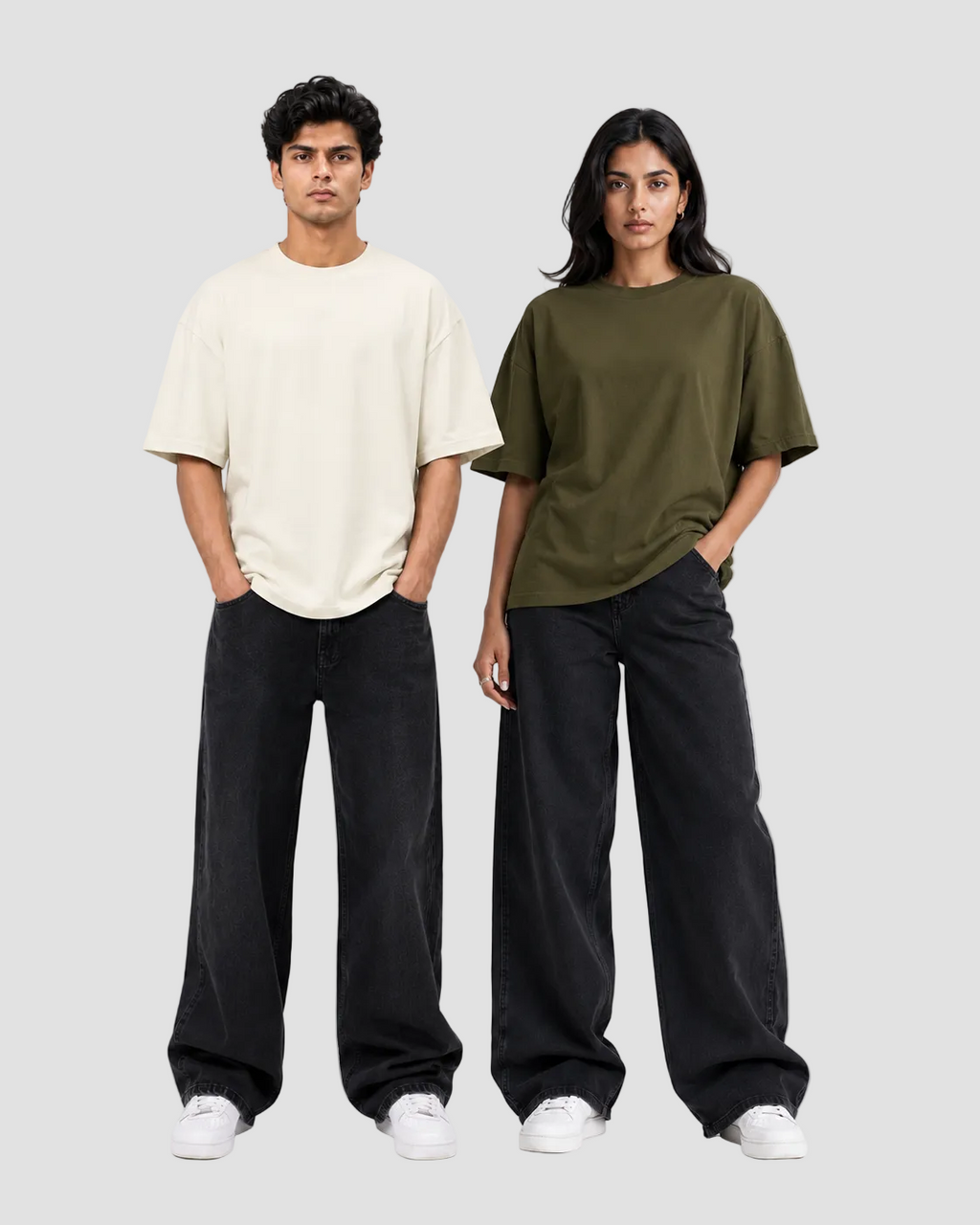 Two models standing against a light gray studio background, each wearing an oversized short-sleeve T-shirt and loose black wide-leg pants with white sneakers. The shirt on the left is off-white/cream, and the shirt on the right is olive green.