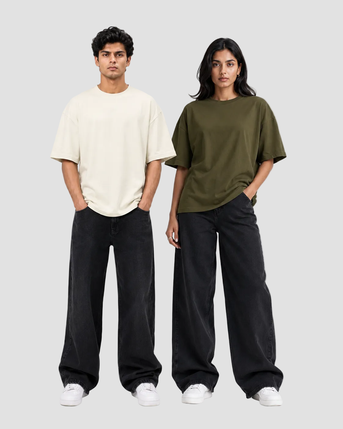 Two models standing against a light gray studio background, each wearing an oversized short-sleeve T-shirt and loose black wide-leg pants with white sneakers. The shirt on the left is off-white/cream, and the shirt on the right is olive green.